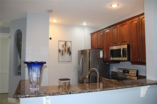 kitchen featuring appliances with stainless steel finishes, dark stone countertops, kitchen peninsula, and sink