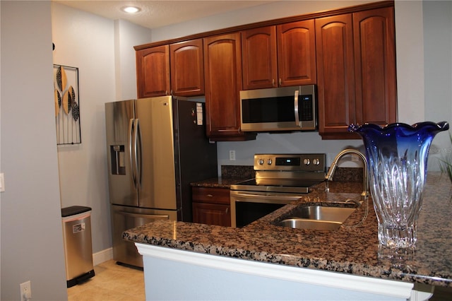 kitchen with appliances with stainless steel finishes, light tile patterned flooring, sink, and dark stone counters