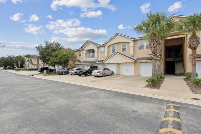 view of property featuring a garage, driveway, stairway, a residential view, and stucco siding