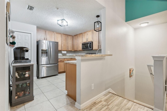 kitchen with stainless steel appliances, light countertops, hanging light fixtures, a textured ceiling, and a peninsula