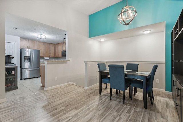 dining space featuring light wood finished floors, baseboards, a chandelier, and a textured ceiling