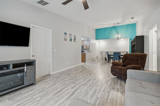 living area with light wood-type flooring, visible vents, baseboards, and ceiling fan with notable chandelier