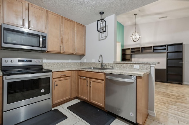 kitchen with appliances with stainless steel finishes, pendant lighting, light countertops, and a sink