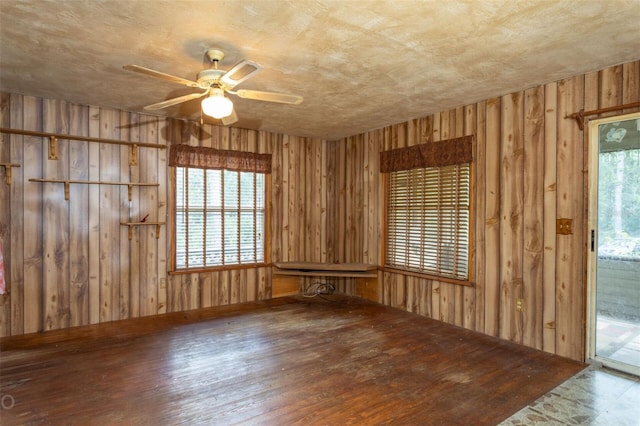 unfurnished room featuring wood walls, plenty of natural light, ceiling fan, and hardwood / wood-style floors