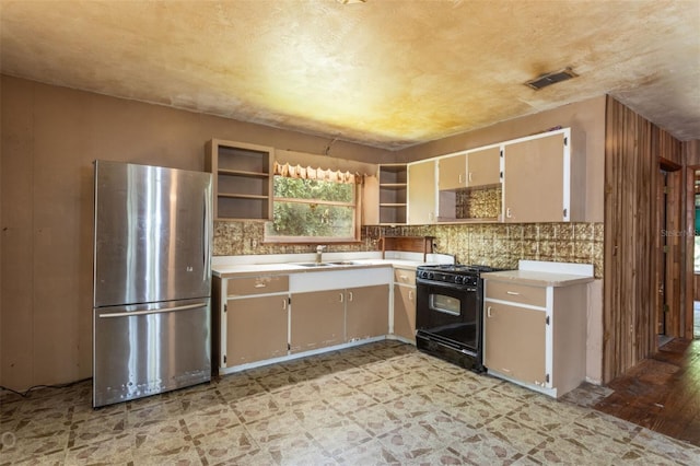 kitchen featuring black range with gas stovetop, light wood-type flooring, stainless steel refrigerator, decorative backsplash, and sink