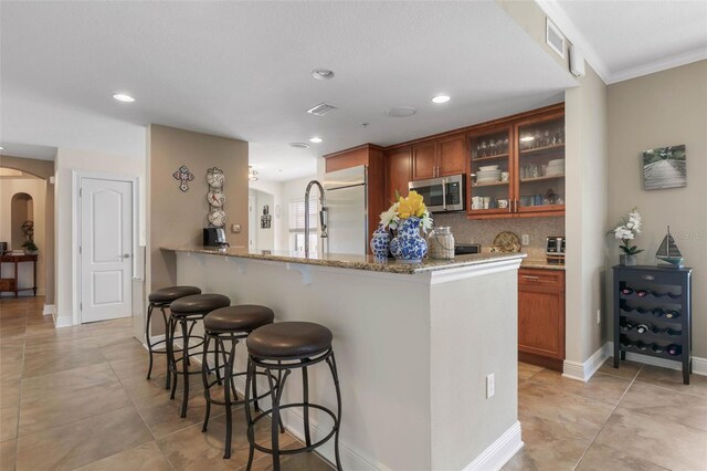 kitchen with light tile patterned flooring, stainless steel appliances, light stone counters, a kitchen bar, and kitchen peninsula