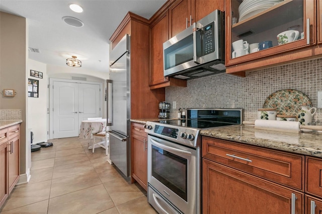 kitchen with appliances with stainless steel finishes, tasteful backsplash, light stone counters, and light tile patterned floors