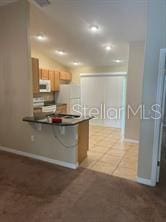 kitchen featuring white appliances, a breakfast bar area, tile patterned flooring, vaulted ceiling, and kitchen peninsula