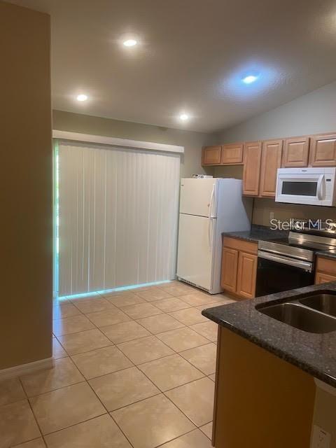 kitchen featuring sink, light tile patterned floors, white appliances, vaulted ceiling, and dark stone counters