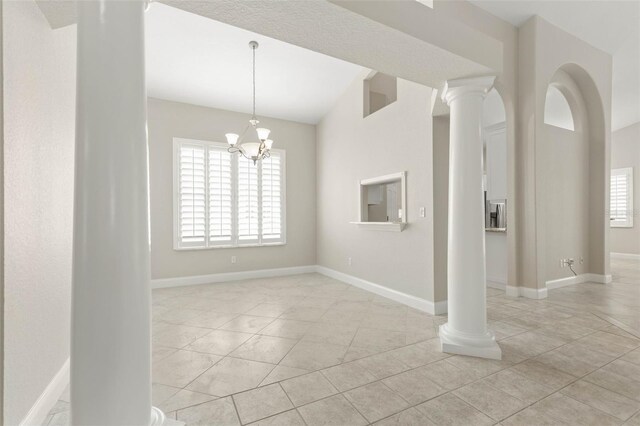 tiled empty room with lofted ceiling, a notable chandelier, and ornate columns