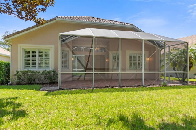 rear view of house with a lawn, glass enclosure, and a patio area