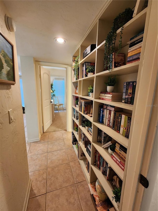 hall featuring light tile patterned flooring and a textured wall