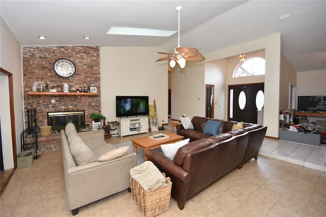 tiled living room featuring a fireplace, a skylight, high vaulted ceiling, brick wall, and ceiling fan