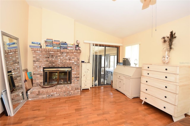 living room with ceiling fan, a brick fireplace, wood-type flooring, and vaulted ceiling