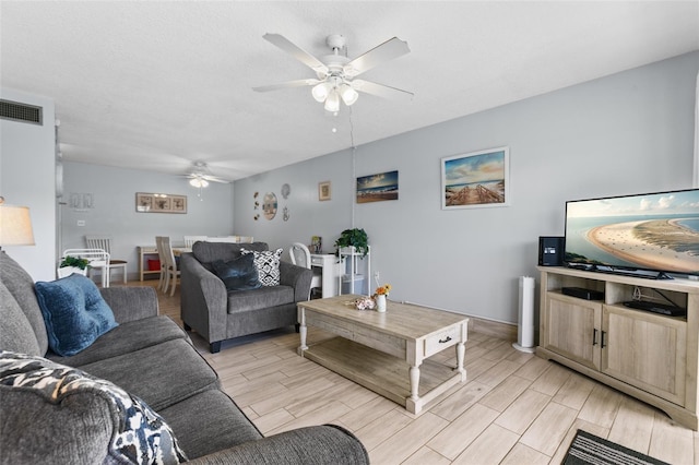 living room featuring wood tiled floor, visible vents, ceiling fan, and a textured ceiling