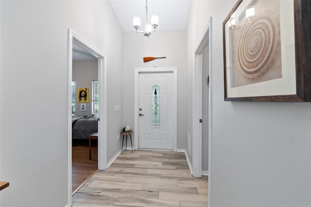 foyer entrance featuring light wood-type flooring, a notable chandelier, and baseboards