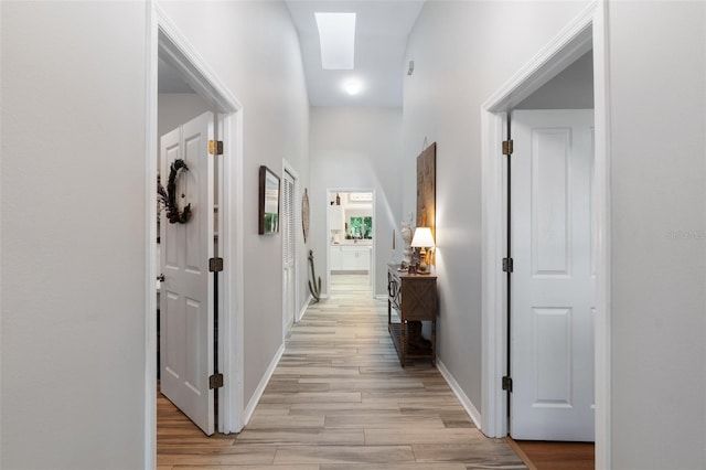 hallway with light wood-type flooring, a skylight, and baseboards