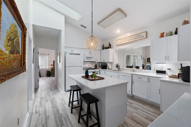 kitchen with white appliances, visible vents, a breakfast bar, light countertops, and white cabinetry