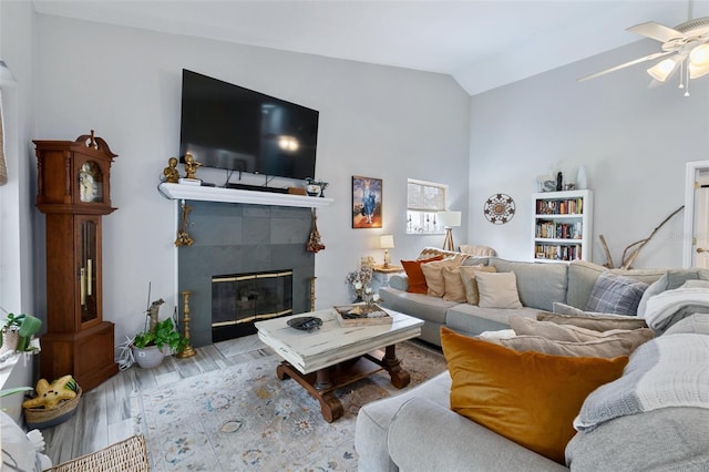 living area featuring a ceiling fan, vaulted ceiling, wood finished floors, and a tile fireplace