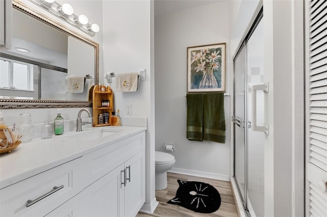 bathroom featuring toilet, a stall shower, vanity, wood finished floors, and baseboards