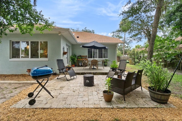 rear view of property featuring a fire pit, fence, roof with shingles, stucco siding, and a patio area