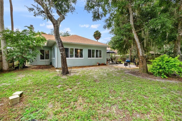 rear view of property featuring a patio area, a lawn, and stucco siding