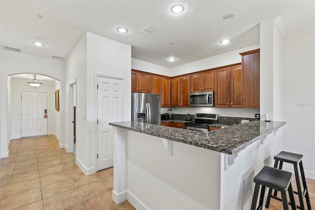 200 Cinnamon Beach Way Unit 122, Palm Coast, FL 32137 - kitchen featuring appliances with stainless steel finishes, arched walkways, a peninsula, a kitchen breakfast bar, and dark stone counters