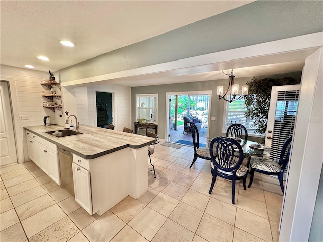 kitchen with light tile patterned floors, hanging light fixtures, sink, white cabinetry, and a chandelier