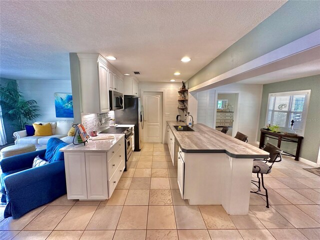 kitchen featuring light tile patterned floors, kitchen peninsula, white cabinets, and stainless steel appliances