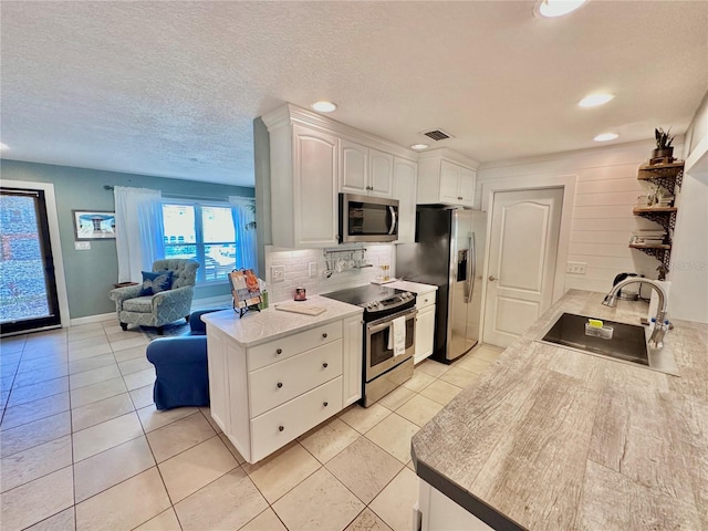 kitchen featuring stainless steel appliances, light tile patterned floors, sink, tasteful backsplash, and white cabinetry