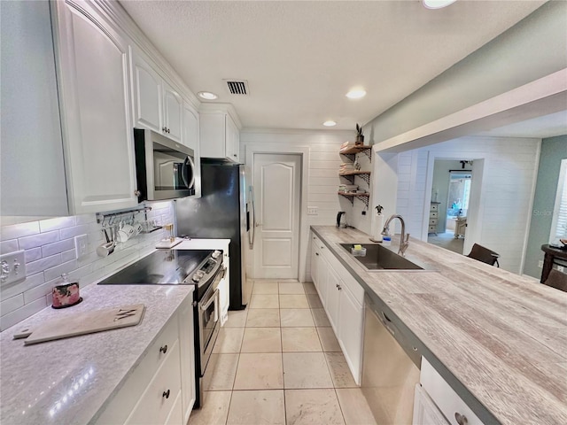 kitchen with appliances with stainless steel finishes, white cabinets, sink, backsplash, and light tile patterned flooring