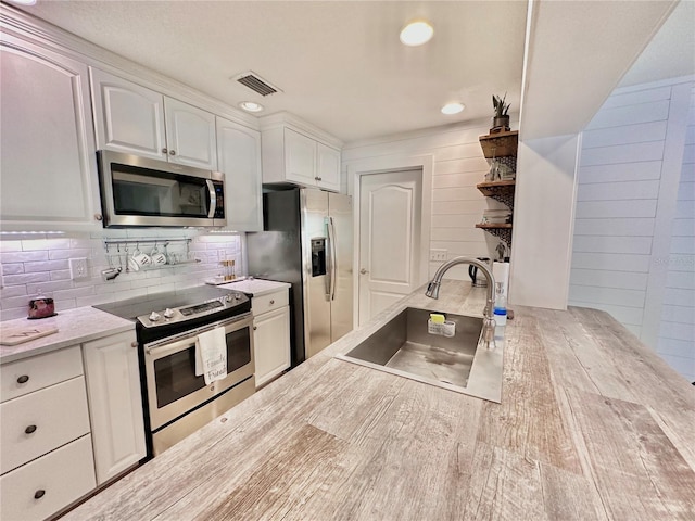 kitchen with hardwood / wood-style floors, appliances with stainless steel finishes, white cabinets, tasteful backsplash, and sink