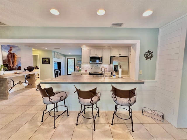 kitchen with stainless steel appliances, light tile patterned floors, a breakfast bar, backsplash, and sink