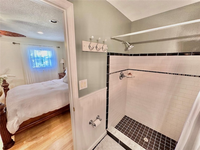 bathroom with a textured ceiling, tiled shower, and wood-type flooring