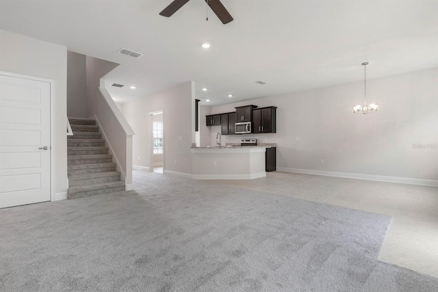 unfurnished living room featuring ceiling fan with notable chandelier and light colored carpet