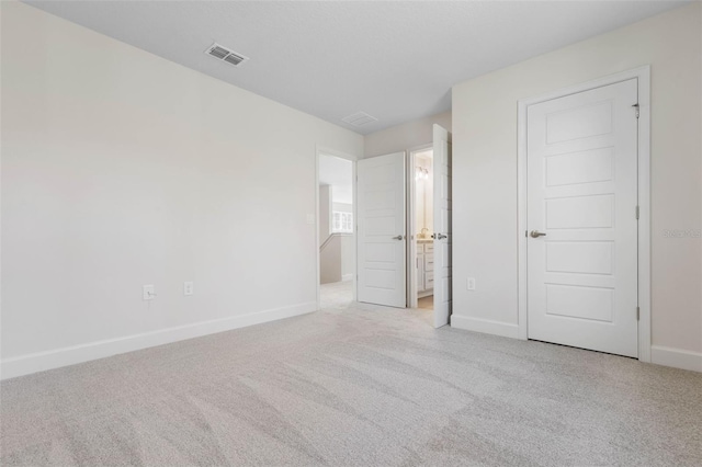 unfurnished bedroom with ensuite bath, baseboards, visible vents, and carpet floors