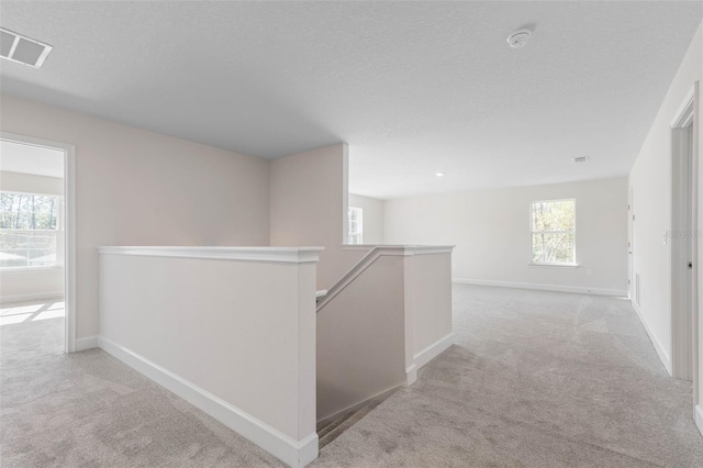 hall featuring visible vents, carpet floors, baseboards, a textured ceiling, and an upstairs landing