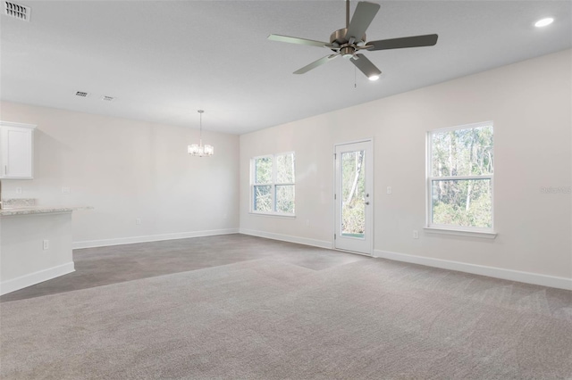 unfurnished living room with carpet, plenty of natural light, ceiling fan with notable chandelier, and visible vents