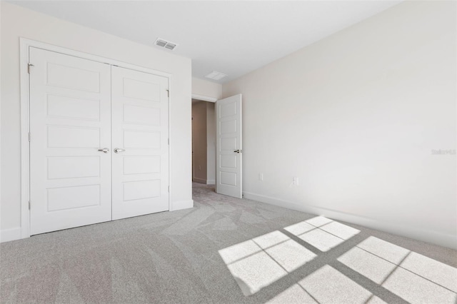 unfurnished bedroom with baseboards, visible vents, light carpet, and a closet