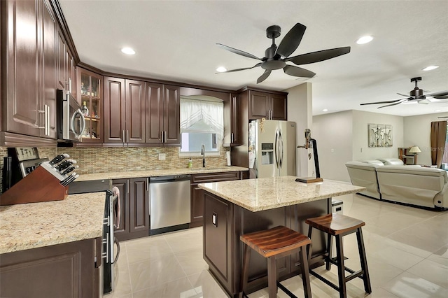 kitchen with a center island, ceiling fan, stainless steel appliances, and light stone counters