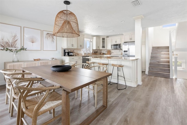 dining room featuring recessed lighting, visible vents, light wood-style floors, stairway, and decorative columns