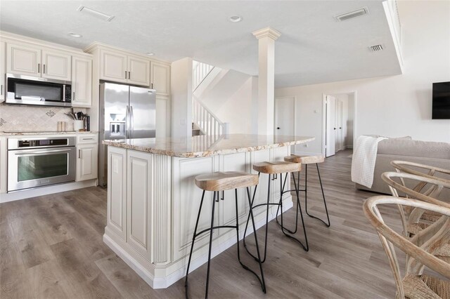 kitchen featuring a center island, light wood-type flooring, appliances with stainless steel finishes, light stone counters, and tasteful backsplash