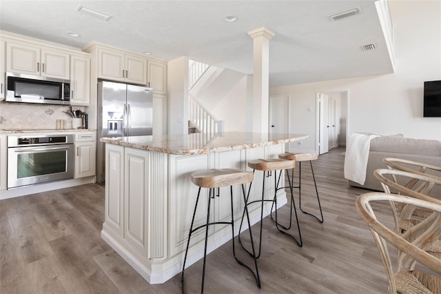 kitchen featuring a center island, stainless steel appliances, a kitchen bar, open floor plan, and ornate columns