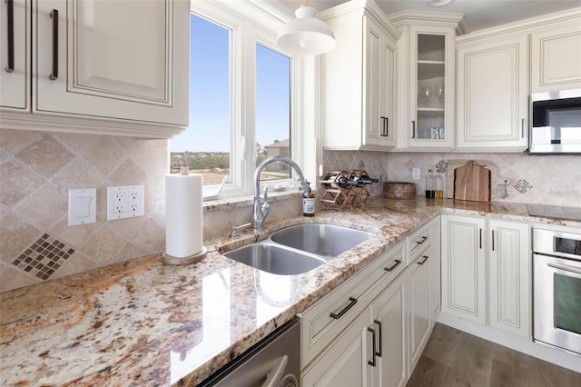 kitchen with tasteful backsplash, glass insert cabinets, appliances with stainless steel finishes, light stone countertops, and a sink