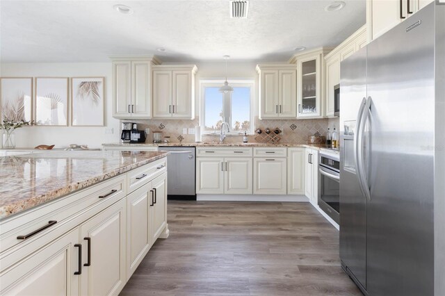 kitchen featuring light wood-type flooring, light stone countertops, stainless steel appliances, pendant lighting, and decorative backsplash