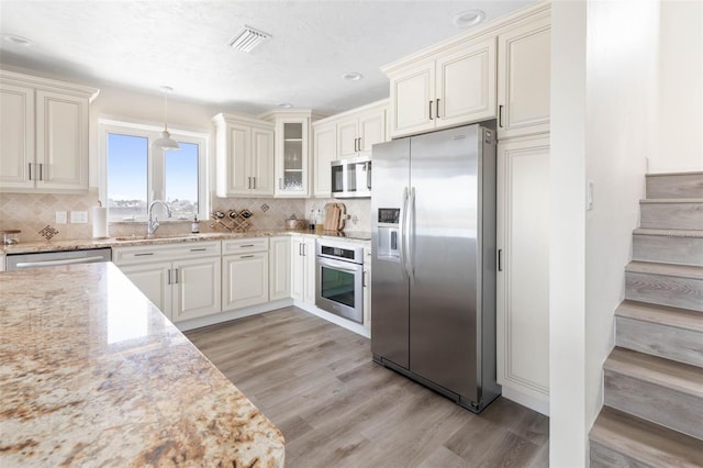 kitchen with pendant lighting, stainless steel appliances, visible vents, glass insert cabinets, and light stone countertops