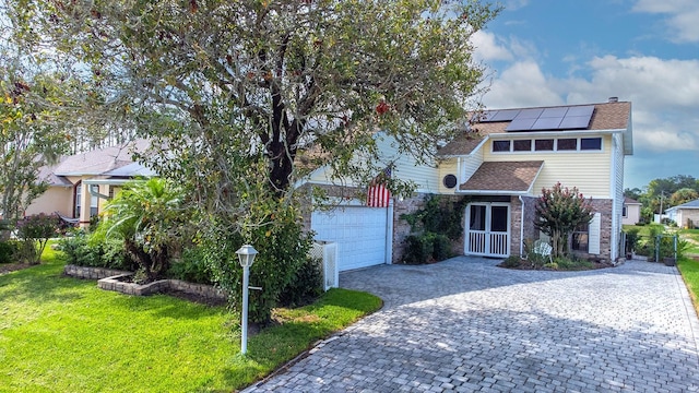 view of property hidden behind natural elements with decorative driveway, brick siding, solar panels, a front yard, and a garage