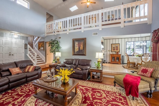 living room with high vaulted ceiling, ceiling fan with notable chandelier, wood finished floors, visible vents, and stairway