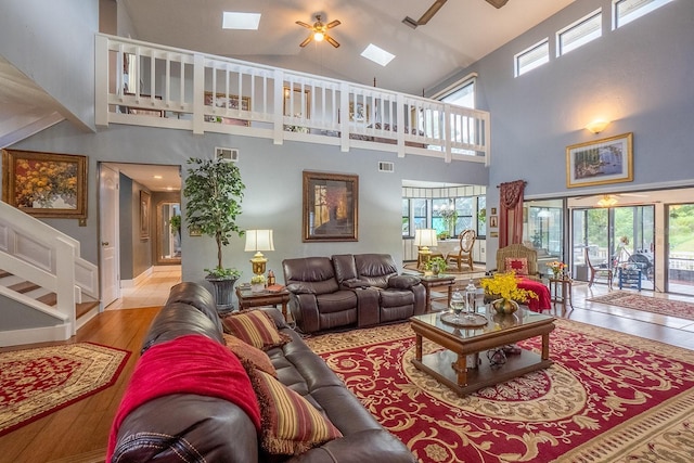 living room featuring ceiling fan, vaulted ceiling with skylight, light wood finished floors, and visible vents