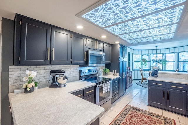 kitchen with light tile patterned floors, light countertops, decorative backsplash, appliances with stainless steel finishes, and dark cabinets